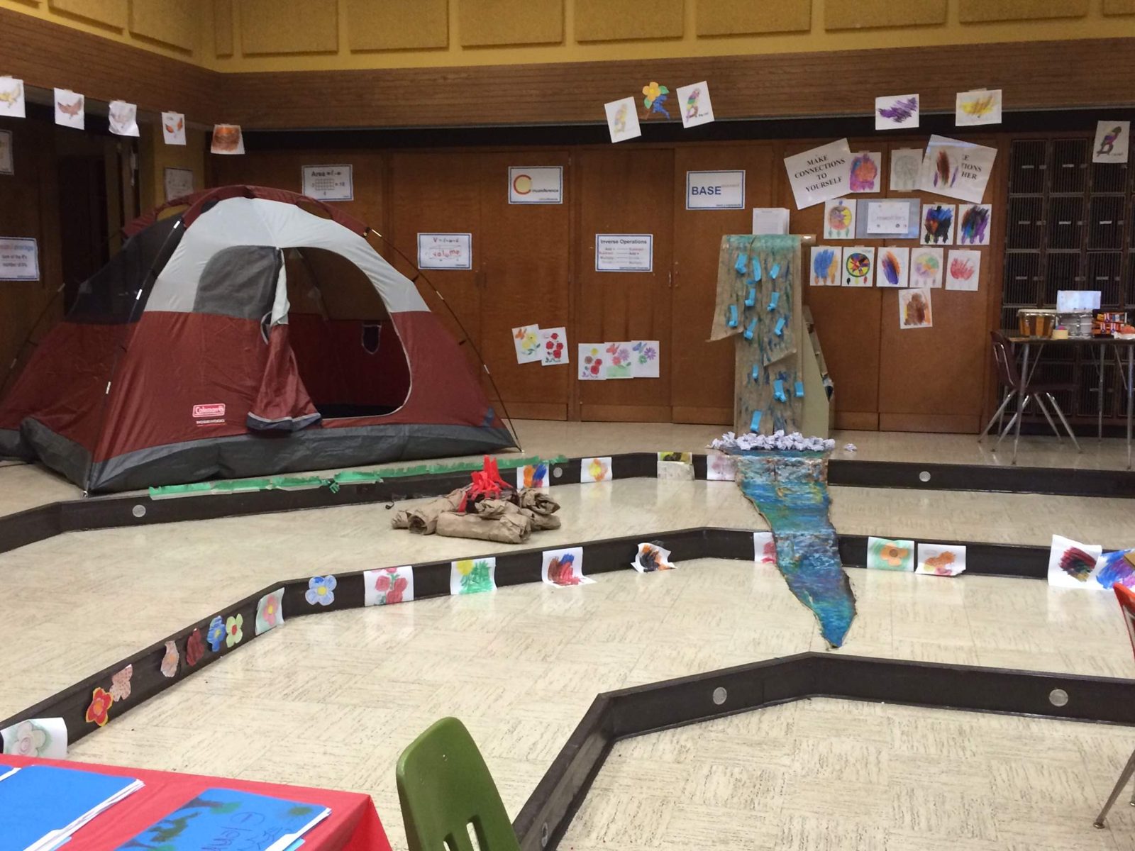 A classroom transformed into a campsite: a tent, a paper campfire, and a painted river lined with student artwork