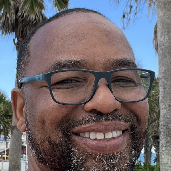 Eli Davis smiling in front of palm trees and the ocean