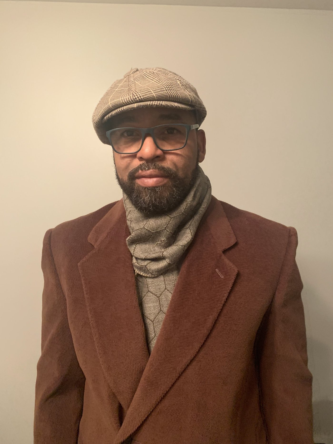 Eli M. Davis in a brown coat, plaid newsboy cap, and patterned scarf